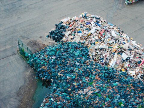 Aerial view of a waste management facility featuring large piles of sorted debris and blue plastic bags on an industrial site in Jurmala, Latvia.