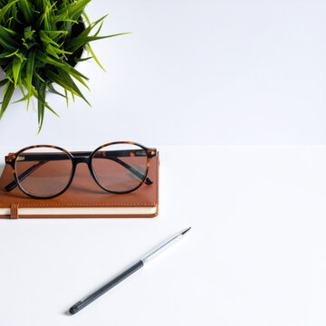 Eyeglass notebook pen plant white background workspace accessory creating clean office composition with practical writing tools and reading eyewear, offering calm organization and generous copy