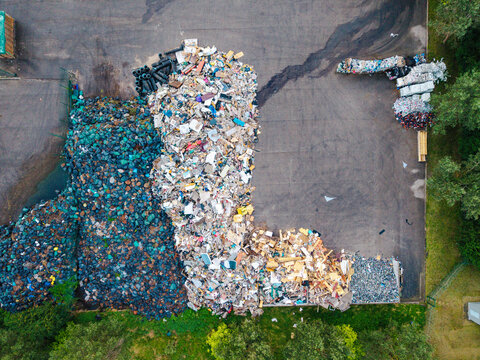 Aerial view of a waste management service facility with large piles of sorted waste, plastic bags, and debris on an asphalt surface in Jurmala, Latvia.