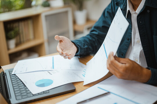 Business professional presents printed charts beside a laptop, communicating financial analysis, organized data, and strategic report findings. Online financial, report; online focus.