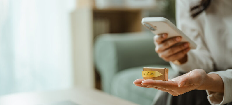 Shopping customer holds a small package while using a smartphone, representing online purchase, mobile payment, and convenient ecommerce delivery. Online return, product; online focus.