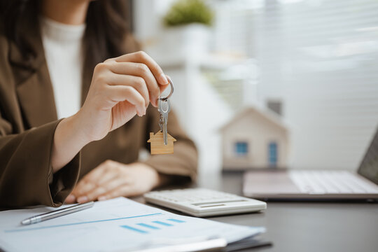 Home buyer holds a key beside a house model and charts, representing property insurance, mortgage approval, and real estate investment for commercial use. Real estate, mortgage; real focus.