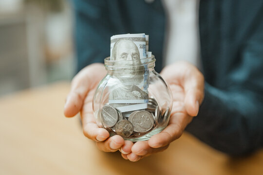 Savings are represented by hands holding a glass jar filled with cash and coins, supporting financial planning, money security, and investment goals. Saving money, savings; saving focus.