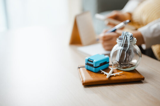 Travel budget still life pairs blue luggage and an airplane with a savings jar, showing vacation preparation and disciplined money planning. Travel savings, vacation; travel focus.