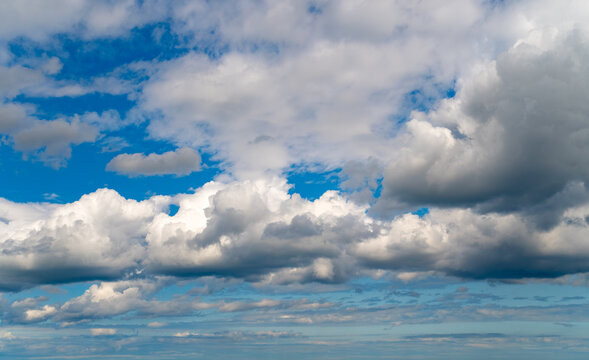 Wide view of a blue sky filled with white and grey cumulus clouds, hazy horizon below. Ideal for sky replacement or background use.