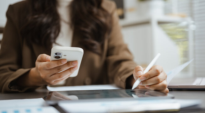 Mobile professional uses a smartphone while writing at a laptop, illustrating digital finance tasks, connected technology, and organized banking work. Using tablet, analysis; using focus.