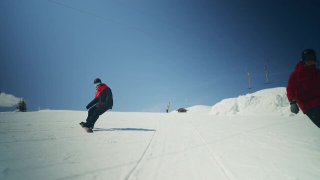 Two snowboarders glide down a snowy mountain under a bright blue sky. Friends enjoy winter sports and adventure on the slopes.