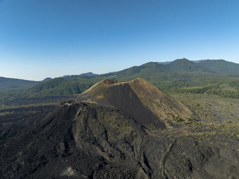 Aerial view of the Paricutin volcano, featuring its dark volcanic cone and solidified lava fields surrounded by green mountains in San Juan Parangaricutiro, Michoacan, Mexico.