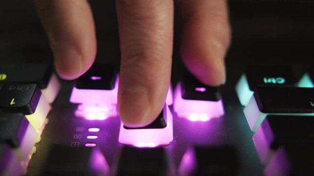 Gamer fingers of hand pressing combination of keys on gaming keyboard with neon purple backlight while playing computer game in dark room close-up