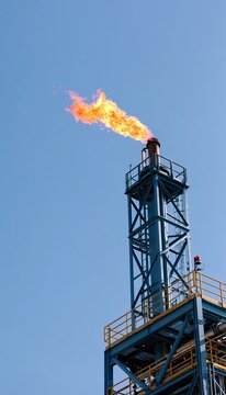 Offshore gas flare stack burning against clear blue sky
