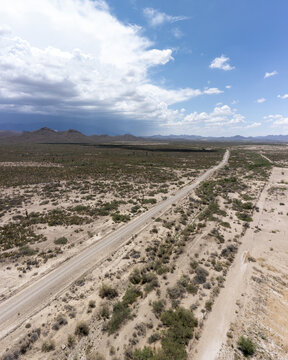 Aerial view of a long dirt road stretching through the arid desert landscape with sparse vegetation and cacti in Parras de la Fuente, Coahuila de Zaragoza, Mexico.