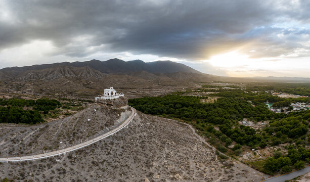 Aerial view of the Church of the Santo Madero on a rocky hill with a winding path, surrounded by arid terrain and lush trees in Parras de la Fuente, Coahuila, Mexico.