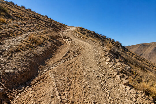 Steep unpaved trail on dry rocky hillside with ruts and exposed roots, arduous hiking path concept