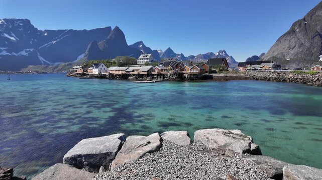 Picturesque fishing village of Reine in the Lofoten Islands, Norway. Traditional red Rorbuer cabins built on stilts over the crystal clear water