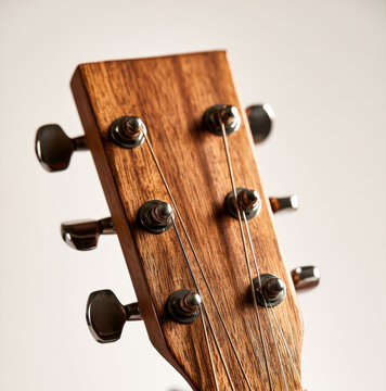 Acoustic guitar headstock close up showing wooden grain tuning pegs and metal strings soft background lighting music instrument detail songwriting audio recording studio equipment concept