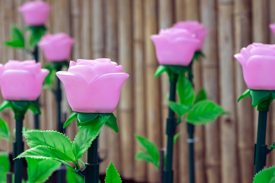 Rows of LED artificial pink rose lights in illuminated garden on artificial snow. LED artificial pink rose lights on dark green stems with fluffy artificial white snow and artificial green grass.
