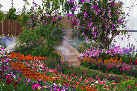 Colorful vibrant indoor flower garden with fountain and artificial stream in modern greenhouse. Concept for landscaping, botanical display, agritourism, and indoor garden design and eco tourism.