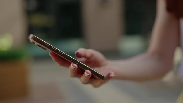 Close-up hand of young woman holding mobile phone and swiping screen with finger. Millennial person texting on modern gadget, browsing social media and shopping online from device, slow motion.