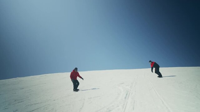 Two snowboarders glide down a vast snowy mountain against a clear blue sky. The scene captures the exhilarating essence of winter sports and outdoor activity.