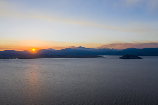 Aerial view of the island of Janitzio in Lake Patzcuaro at sunset, with mountains in the background and calm water reflecting the golden light in Janitzio, Michoacan, Mexico.