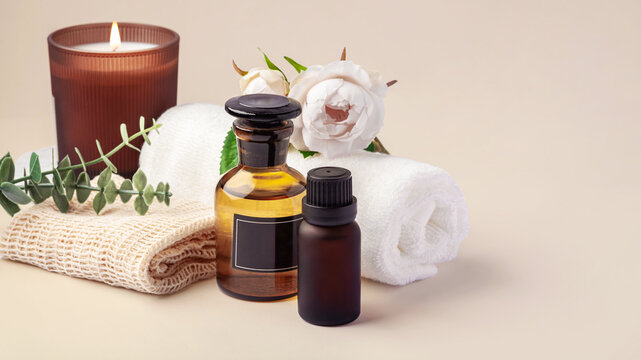 Spa and wellness composition with essential oil, aroma burning candles, and towels on beige background, copy space
