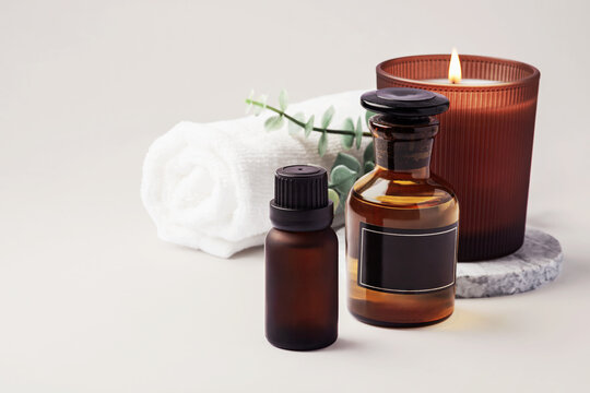 Spa background with a burning aromatherapy candle, essential oil bottles and green leaves, copy space