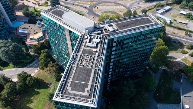 Aerial view of the Eni S.p.A. 2 Palazzo Uffici building with its Y-shaped glass facade, rooftop mechanical installations, and surrounding green areas in San Donato Milanese, Lombardia, Italy.