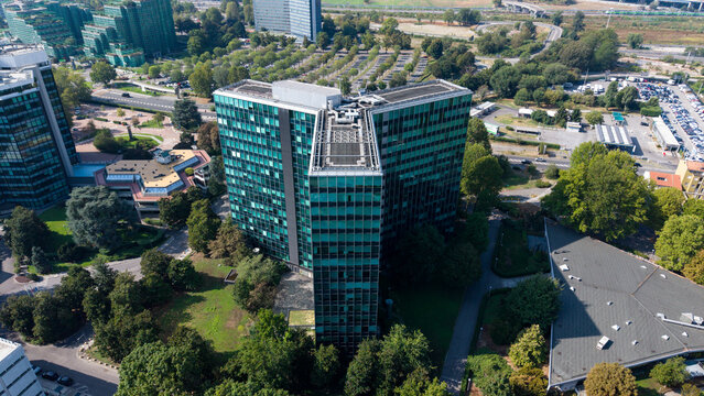 Aerial view of the Eni S.p.A. 2nd Office Building surrounded by lush green trees, parking areas, and modern office structures in San Donato Milanese, Lombardia, Italy.