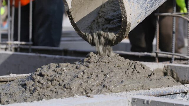 Wet concrete mix pouring from a concrete mixer chute into a reinforced formwork, creating a building foundation on a construction site during a housing project