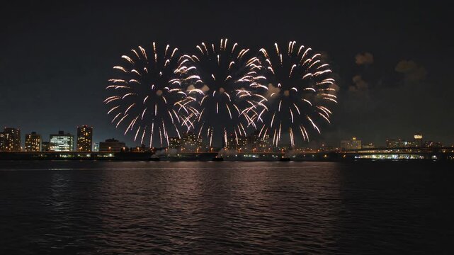 Spectacular fireworks bursting in the night sky over a city river, illuminating the urban skyline and water with beautiful reflections for a festive celebration