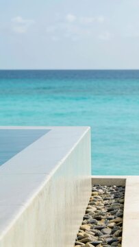 Vertical video: Camera framing infinity pool edge by sea with sun glinting on ledge, water flowing