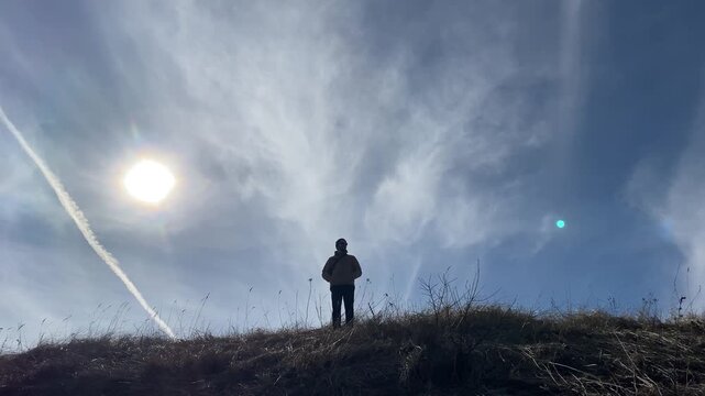 The silhouette of a man on a hill against a backdrop of a blue sky and the sun. An atmospheric scene. Active lifestyle, travel, freedom, and hiking