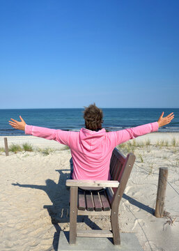 Relaxing Coastal Escape with Woman Sitting on a Wooden Beach Bench