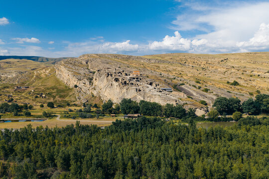 Aerial view of the ancient rock-hewn town of Uplistsikhe, featuring historic cave structures in sandstone cliffs, surrounded by trees and the Mtkvari River in Kvakhvreli, Shida Kartli, Georgia.
