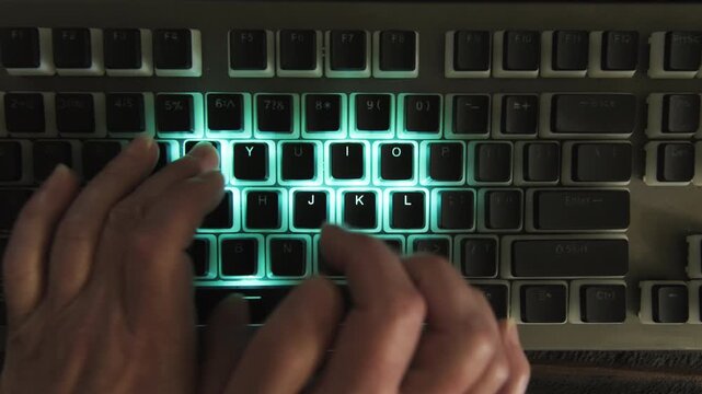 Woman hand typing on computer keyboard with LED backlight in dark room close-up top view