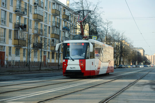 Modern red and white tram driving on a Saint Petersburg street against a yellow residential building. 2025.