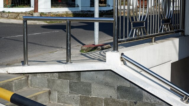 Modern shiny metal guardrail fence installed beside an outdoor building entrance and paved road.