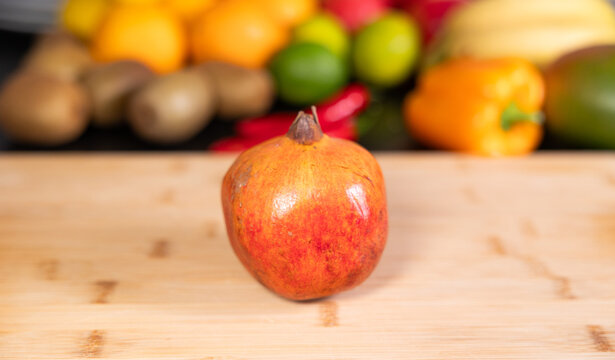 Pomegranate on a cutting board in the kitchen. Fruits and vegetable in the background. Raw food, healthy eating, vegetarian food, oragnic, ripe, ready to eat.