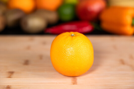 Orange on a cutting board in the kitchen. Fruits and vegetable in the background. Raw food, citrus fruit, healthy eating, organic, ripe, vegetarian food,  ready to eat.