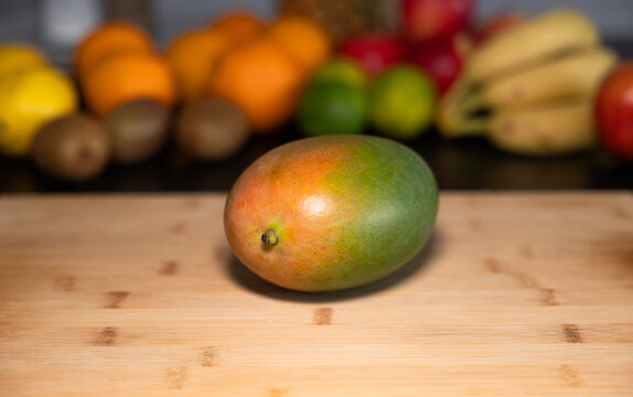 Mango on a cutting board in the kitchen. Fruits and vegetable in the background. Raw food, healthy eating, vegatrian food, organic,  ripe, ready to eat.