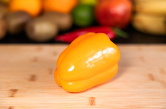 Yellow paprika on a cutting board in the kitchen. Fruits and vegetable in the background. Healthy eating, vegatrian food, preparing a meal, organic, raw food.