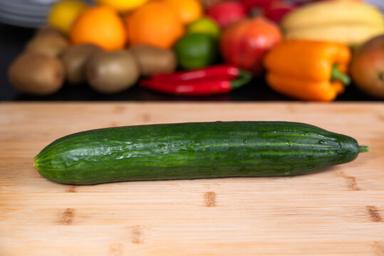 Cucumber on a cutting board in the kitchen. Fruits and vegetable in the background. Healthy eating, vegetarian food, preparing a meal, organic, raw food.
