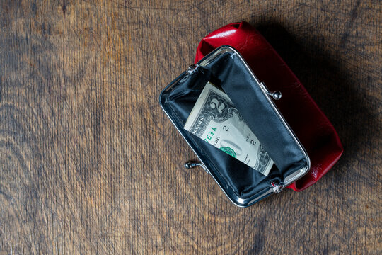 Open retro red leather purse showing folded US dollar bills inside, placed on dark rustic wooden background, closeup. Concept of poverty, savings, financial crisis or daily expenses