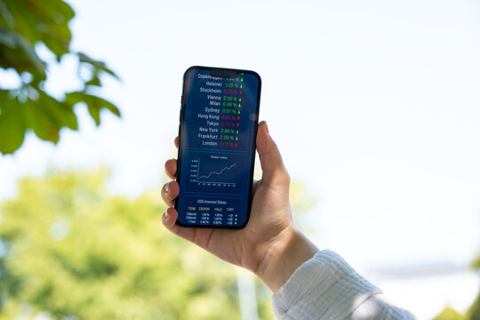 Woman holding up a smartphone displaying stock market data, trading information and chart. Stockbroker, investment decision, stock prices, financial advisor, assets, wealth.