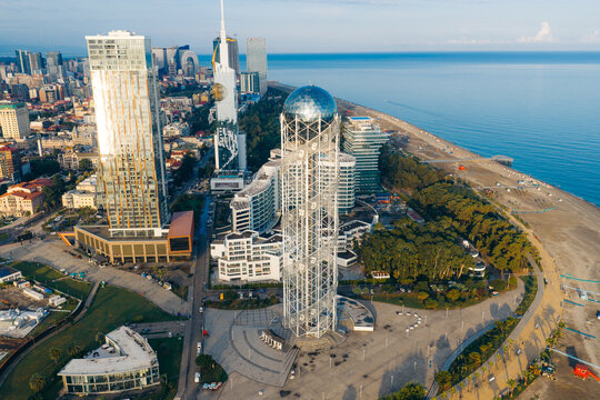 Aerial view of the Alphabet Tower surrounded by modern skyscrapers, lush parkland, and the Black Sea coastline in Batumi, Adjara, Georgia.