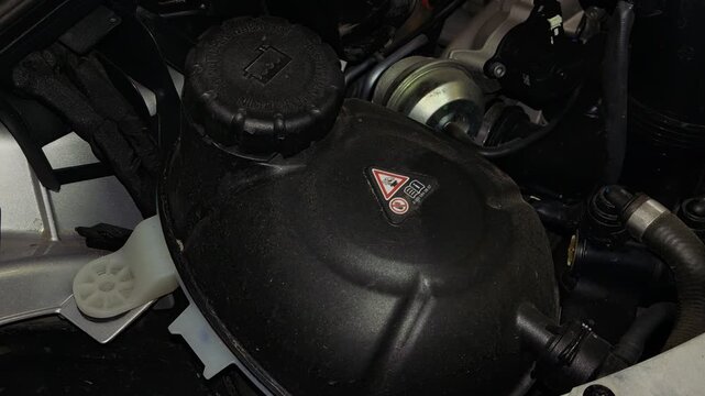 A black plastic coolant expansion tank with a warning label under the hood of a car.