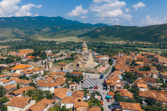 Aerial view of the historic Svetitskhoveli Cathedral surrounded by terracotta rooftops and lush mountains in Mtskheta, Mtskheta-Mtianeti, Georgia.