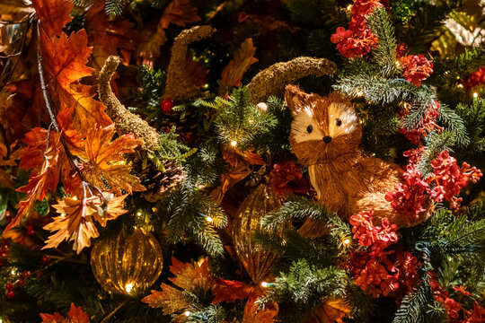 Forest-style Christmas decorations with yellow leaves between tree branches and a fox figurine, selective focus. A beautiful Christmas tree with red flowers and gold glitter.