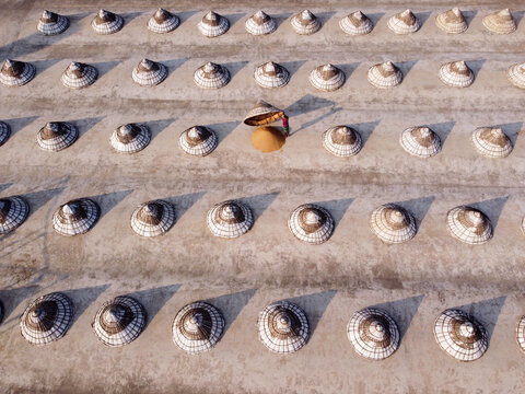 Aerial view of rows of traditional wooden conical paddy storage structures with a worker tending to a pile of harvested grain in Brahmanbaria, Chittagong Division, Bangladesh.