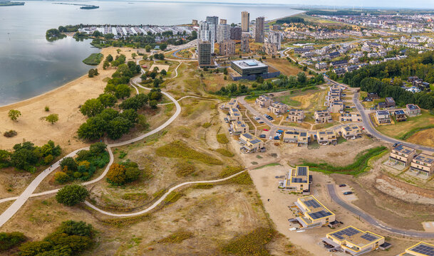 Aerial view of Almere Poort featuring modern residential buildings, winding pathways, sandy beach, and waterfront in Almere, Flevoland, Netherlands.